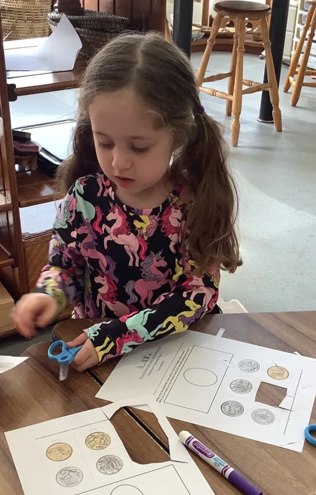 A preschooler sorting printed coins across two money worksheets at a table.